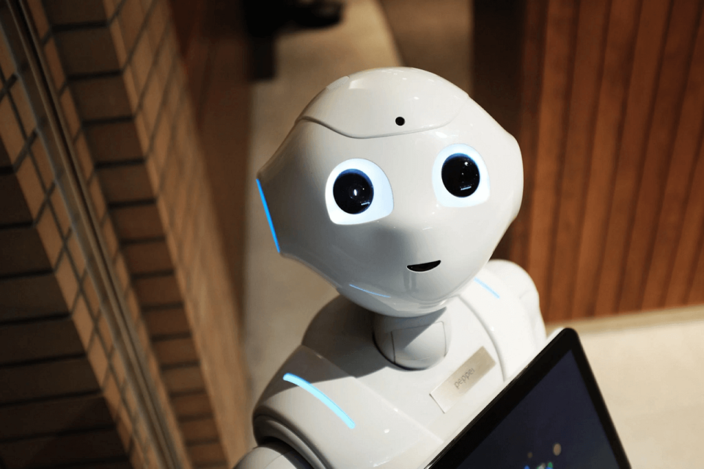 Fotografia białego humanoidalnego robota z dużymi okrągłymi oczami, trzymającego tablet